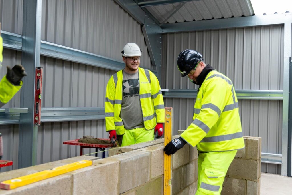 Teacher and pupil building a wall in high vis jackets at the Aspire Academy